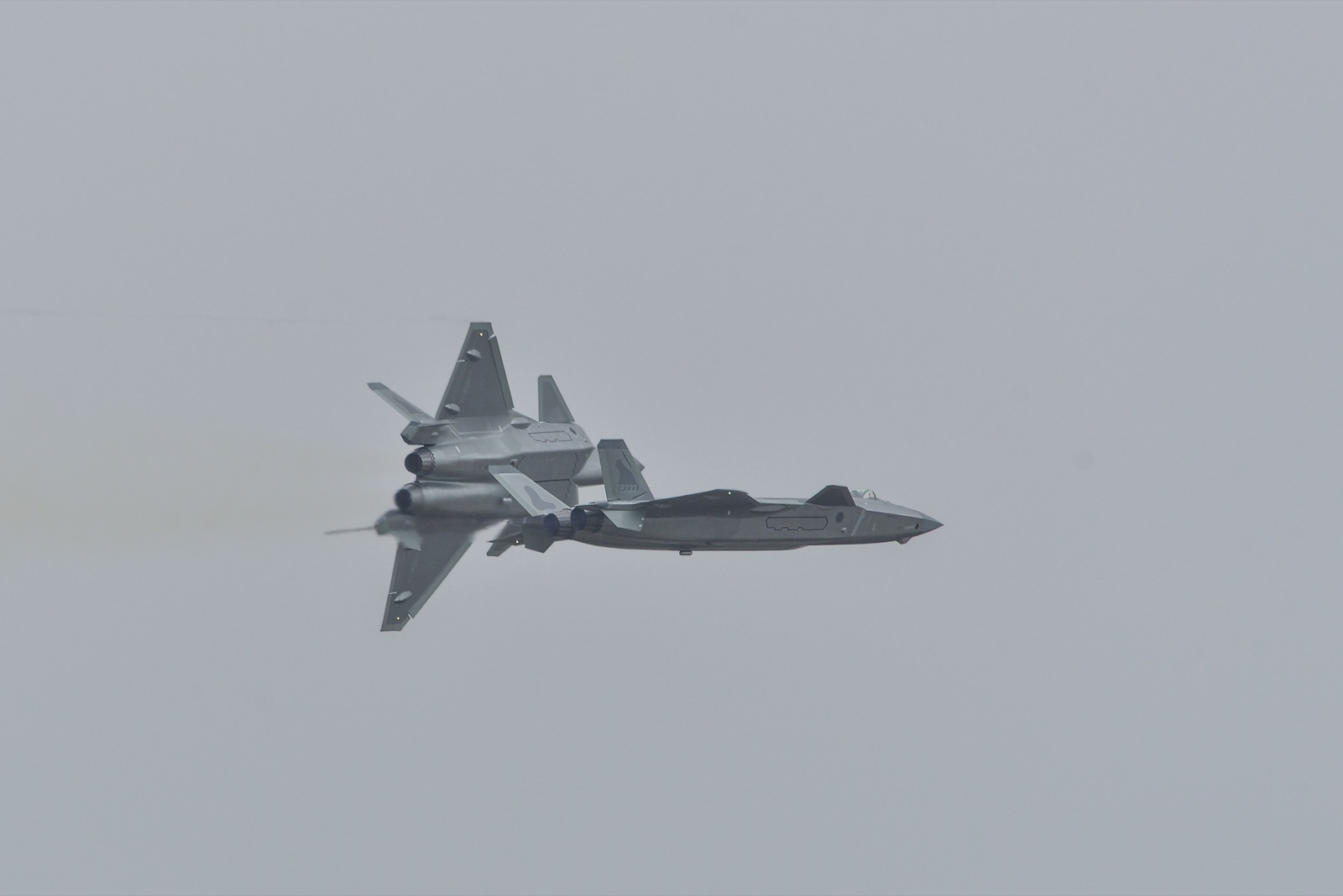 Two grey Chengdu J-20 stealth fighters crossing in a tight display manoeuvre against an overcast sky