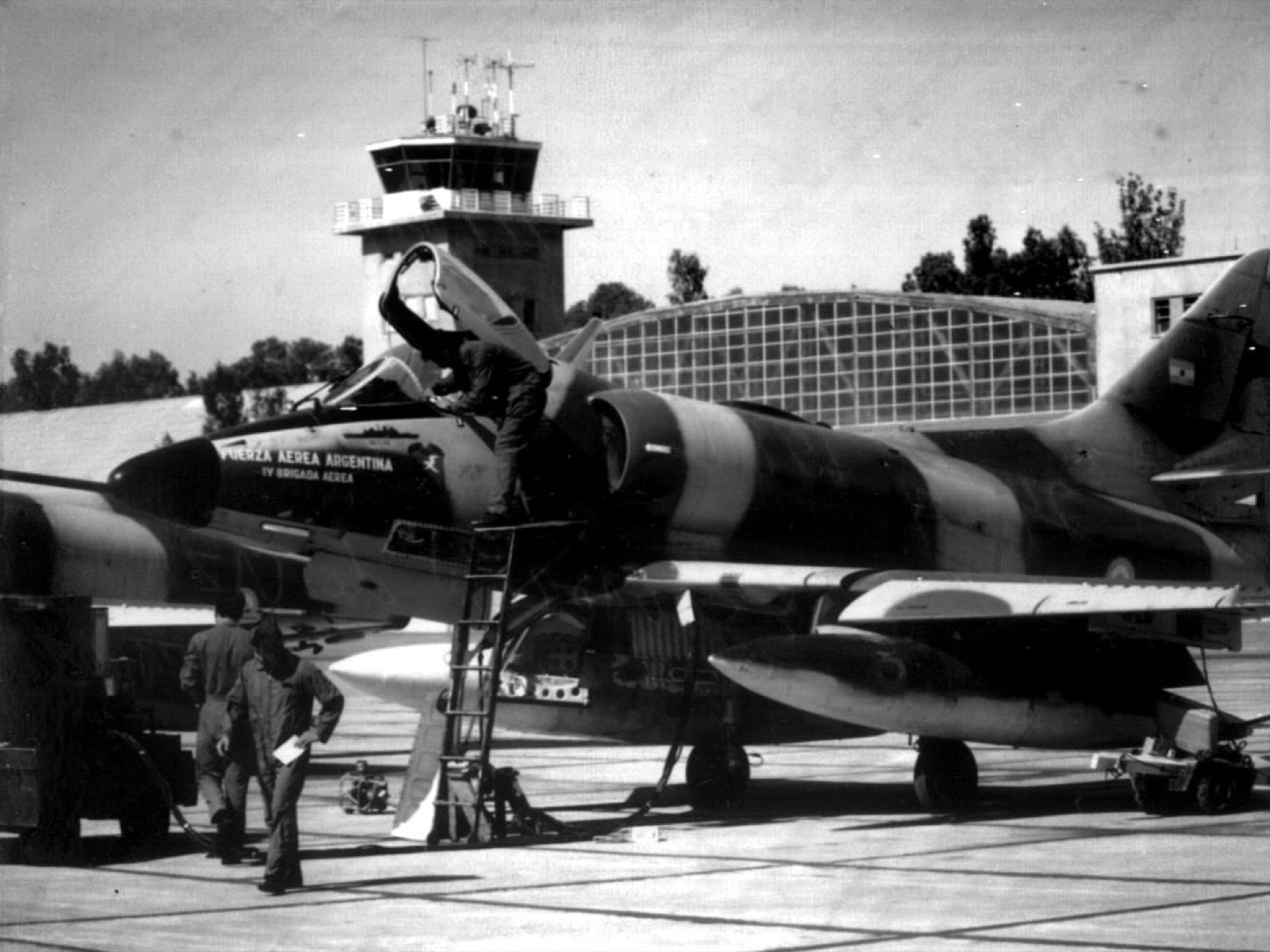 A camouflaged Argentine Air Force A-4C Skyhawk with its canopy open and a pilot climbing in, control tower behind