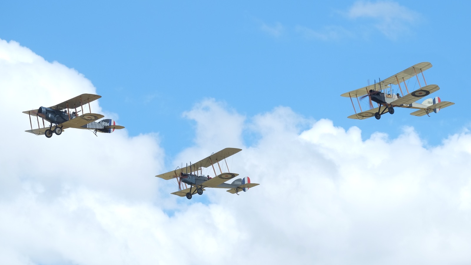Three First World War biplanes flying in loose formation against blue sky and white cloud, all with roundels on their wings