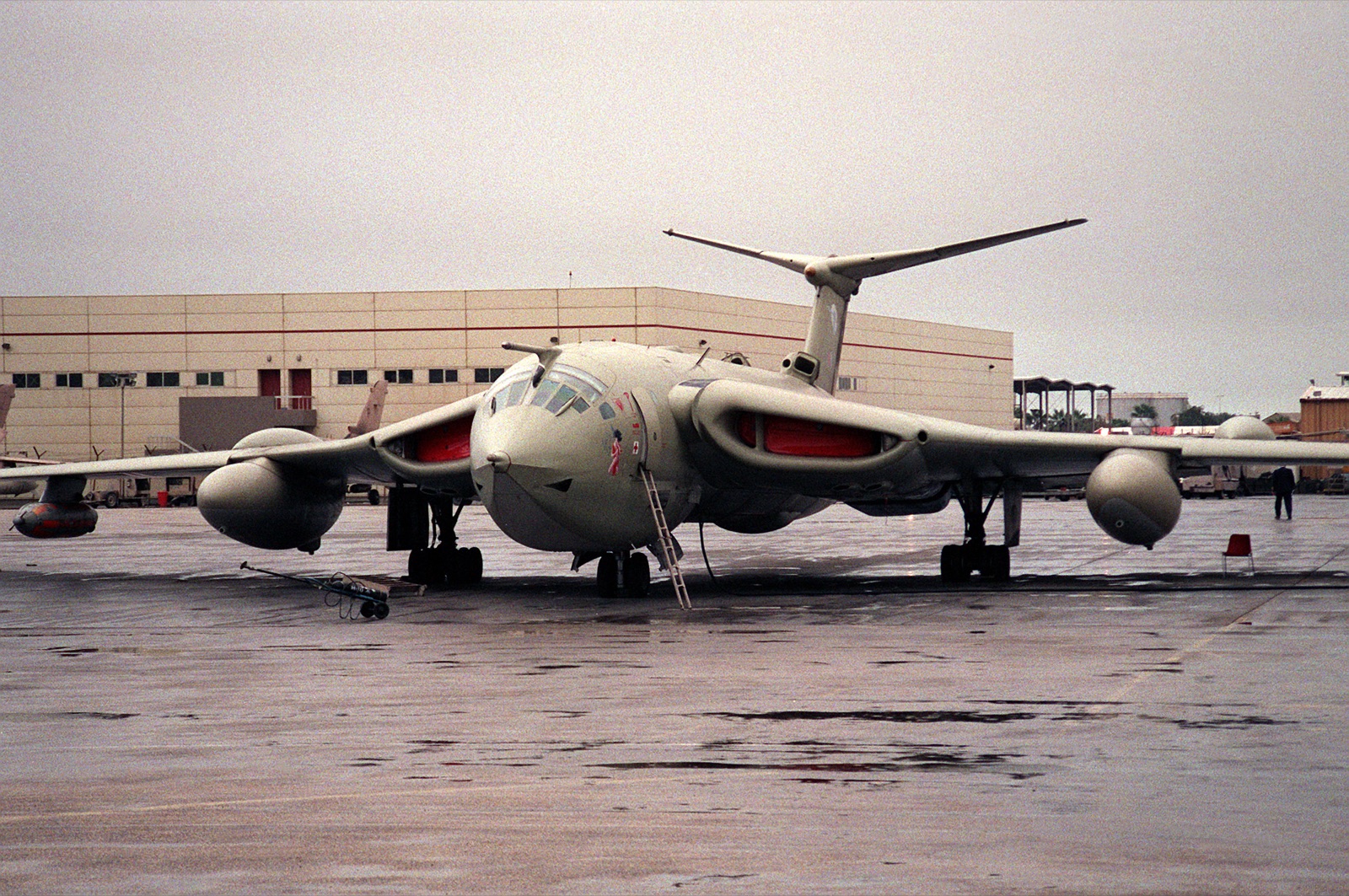 A grey Handley Page Victor tanker with large underwing refuelling pods parked on a wet apron
