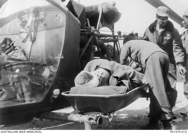 A wounded Australian soldier on a stretcher being loaded into the external pod of a US Army Bell H-13 helicopter.