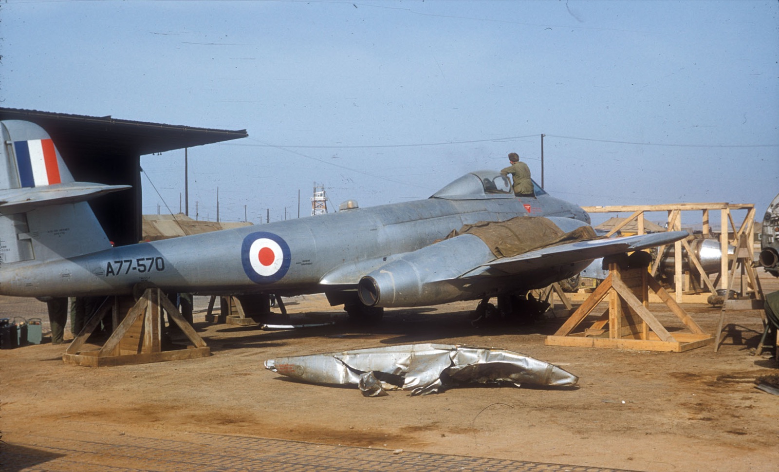 A silver Gloster Meteor F.8 of No. 77 Squadron RAAF, serial A77-570, raised on wooden trestles at Kimpo with a crumpled external fuel tank on the ground beside it.
