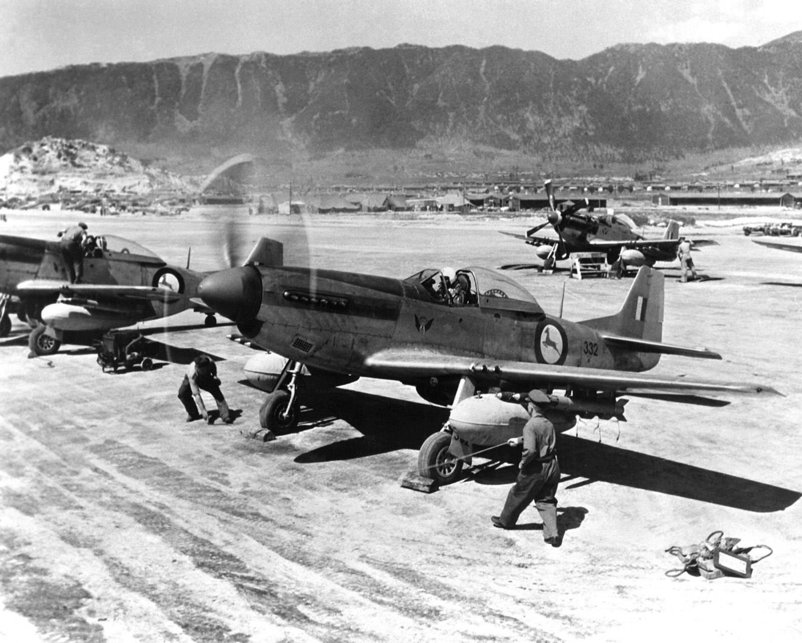 F-51D Mustangs of No. 2 Squadron South African Air Force on a Korean airstrip; a pilot sits in the cockpit of the nearest, number 332, as ground crew prepare it.