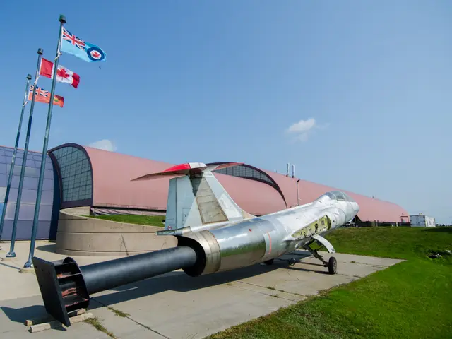 Silver CF-104 Starfighter jet mounted on a pylon outside the museum, beside flagpoles flying Canadian and RCAF flags