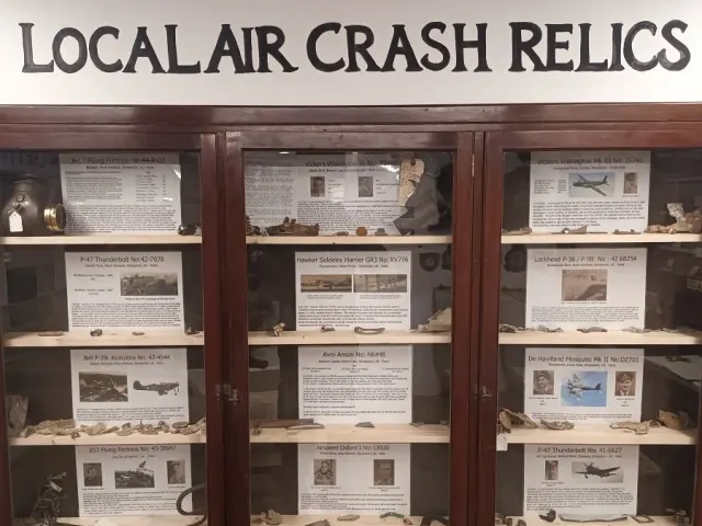 Wooden display cabinets of small aircraft fragments and labels beneath a sign reading Local Air Crash Relics