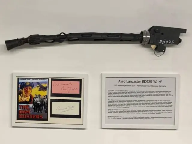 A Browning machine gun mounted on a white wall above a framed Dam Busters display and an information panel