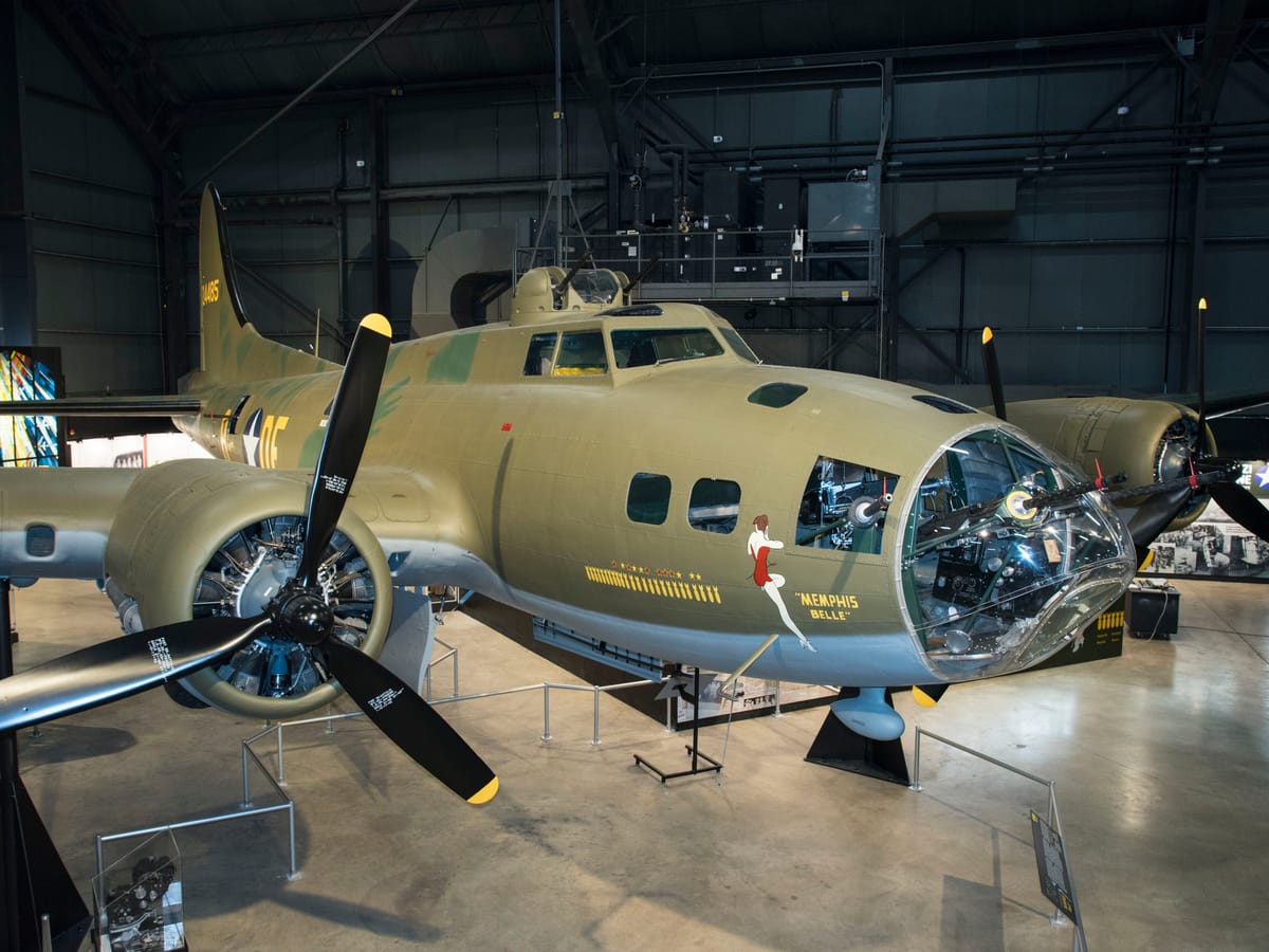 The olive-drab B-17F Memphis Belle, with her nose art, on display in a large museum hangar