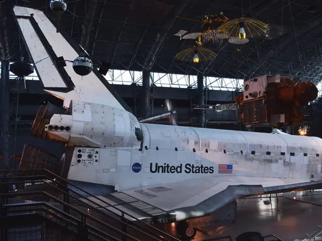 Space Shuttle Discovery seen from the front quarter in the McDonnell Space Hangar, with satellites hung above