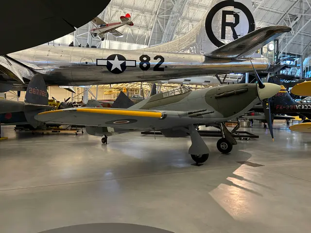 Camouflaged RAF Hawker Hurricane IIC on the hangar floor beneath the tail of the Enola Gay
