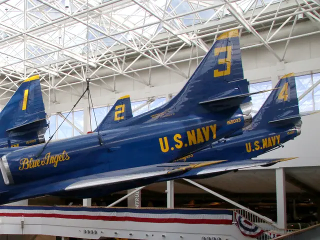 Four blue and gold A-4 Skyhawk jets suspended in diamond formation beneath a glass atrium roof
