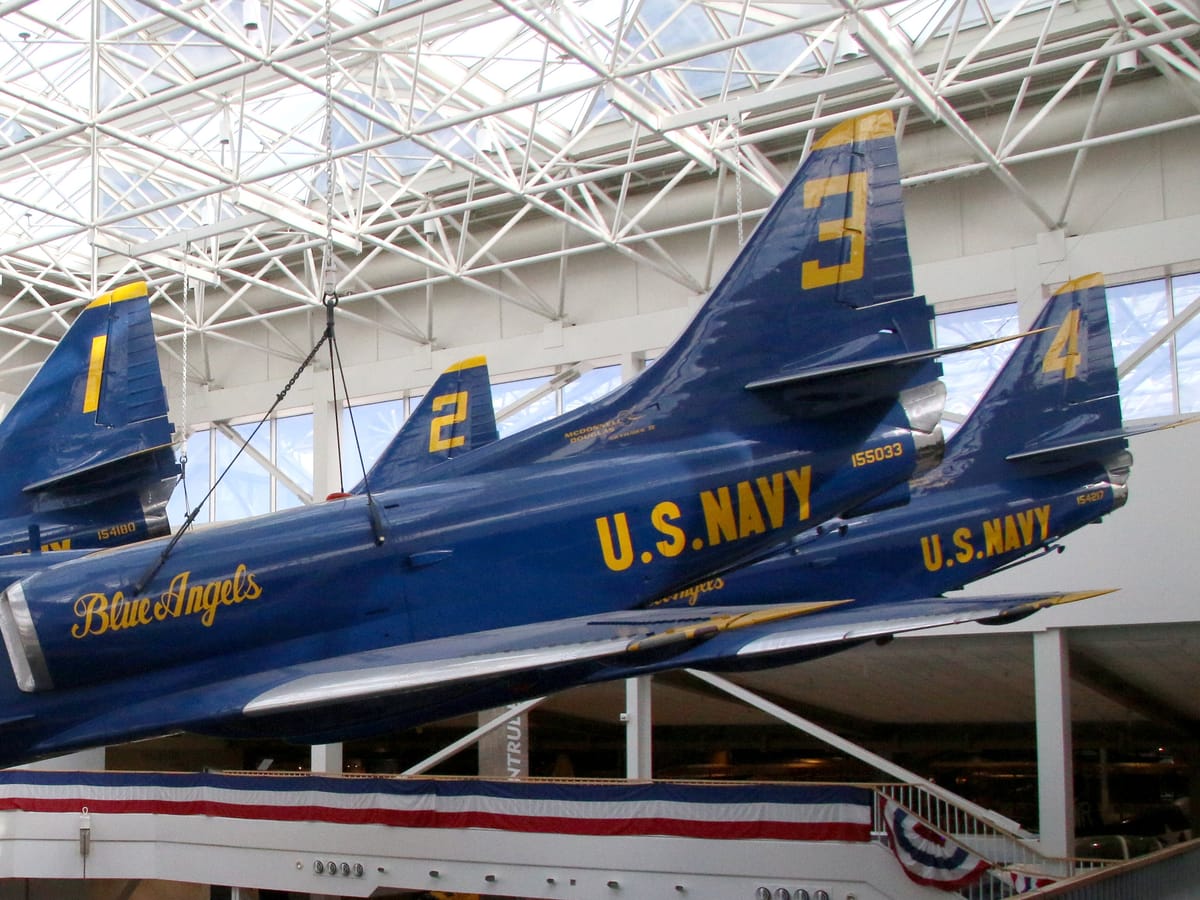 Four blue and gold A-4 Skyhawk jets suspended in diamond formation beneath a glass atrium roof