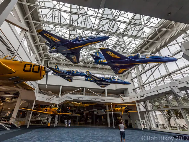 Wide view of a glass-roofed atrium with blue jets and a yellow trainer suspended overhead