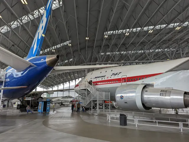 The red-striped first Boeing 747 beside the tail of the third Boeing 787 under a steel roof