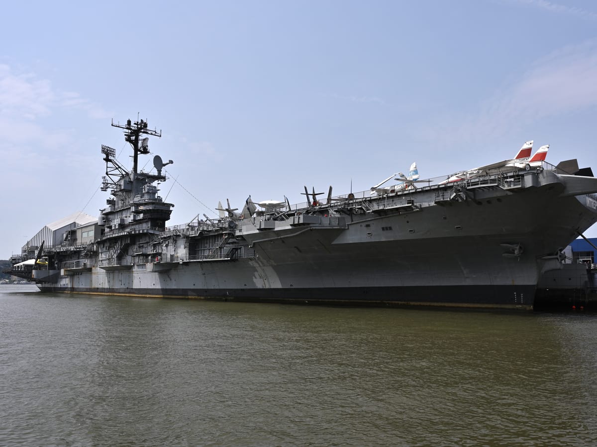 The grey aircraft carrier Intrepid moored on the Hudson, its island superstructure at left and jets parked along the flight deck