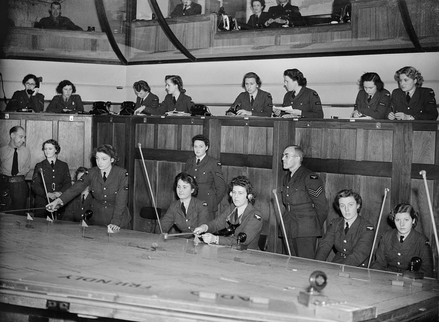WAAF plotters with long rakes around a large map table, with controllers watching from a glazed gallery above